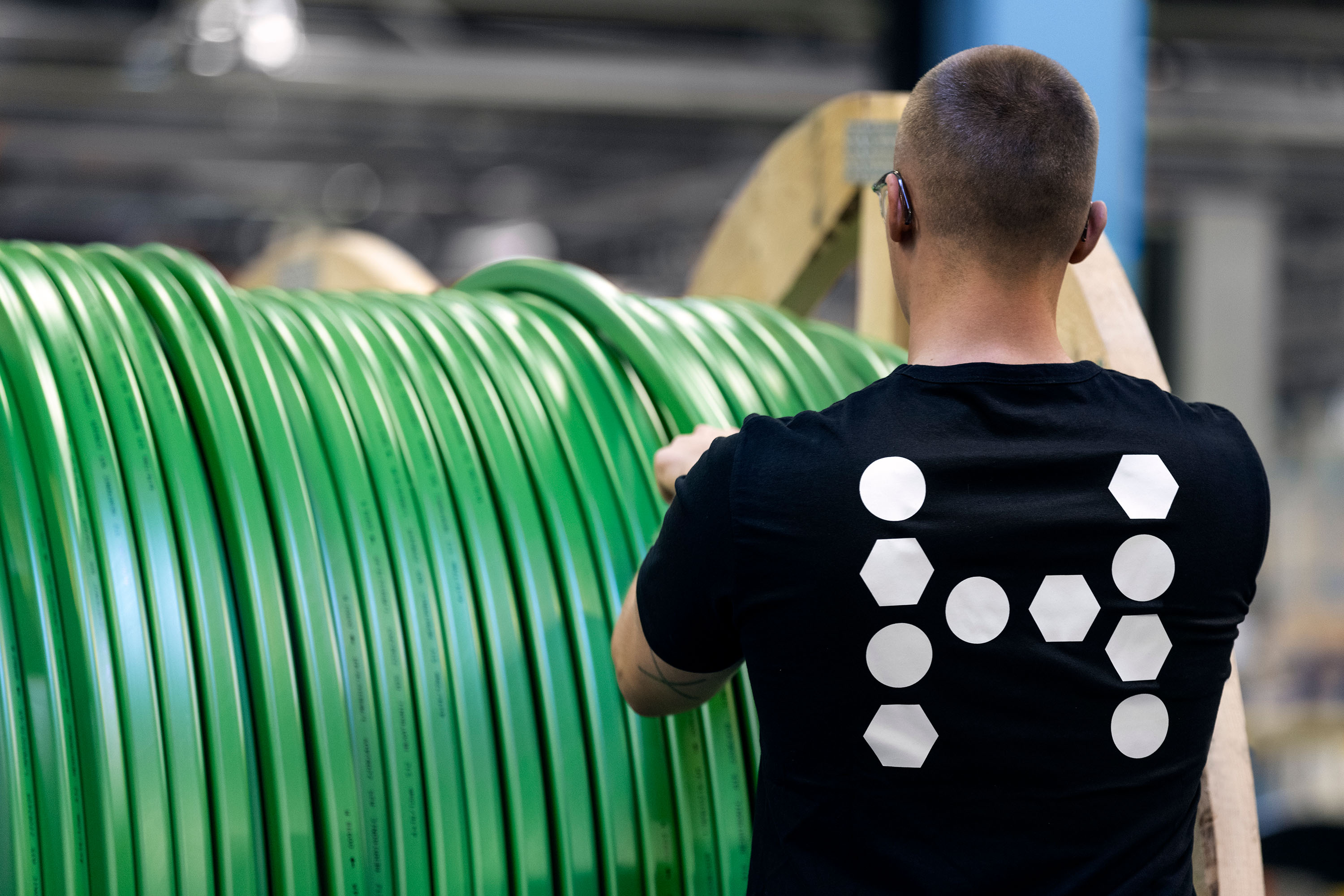 A worker in a factory handling a large spool of bright green micro duct.