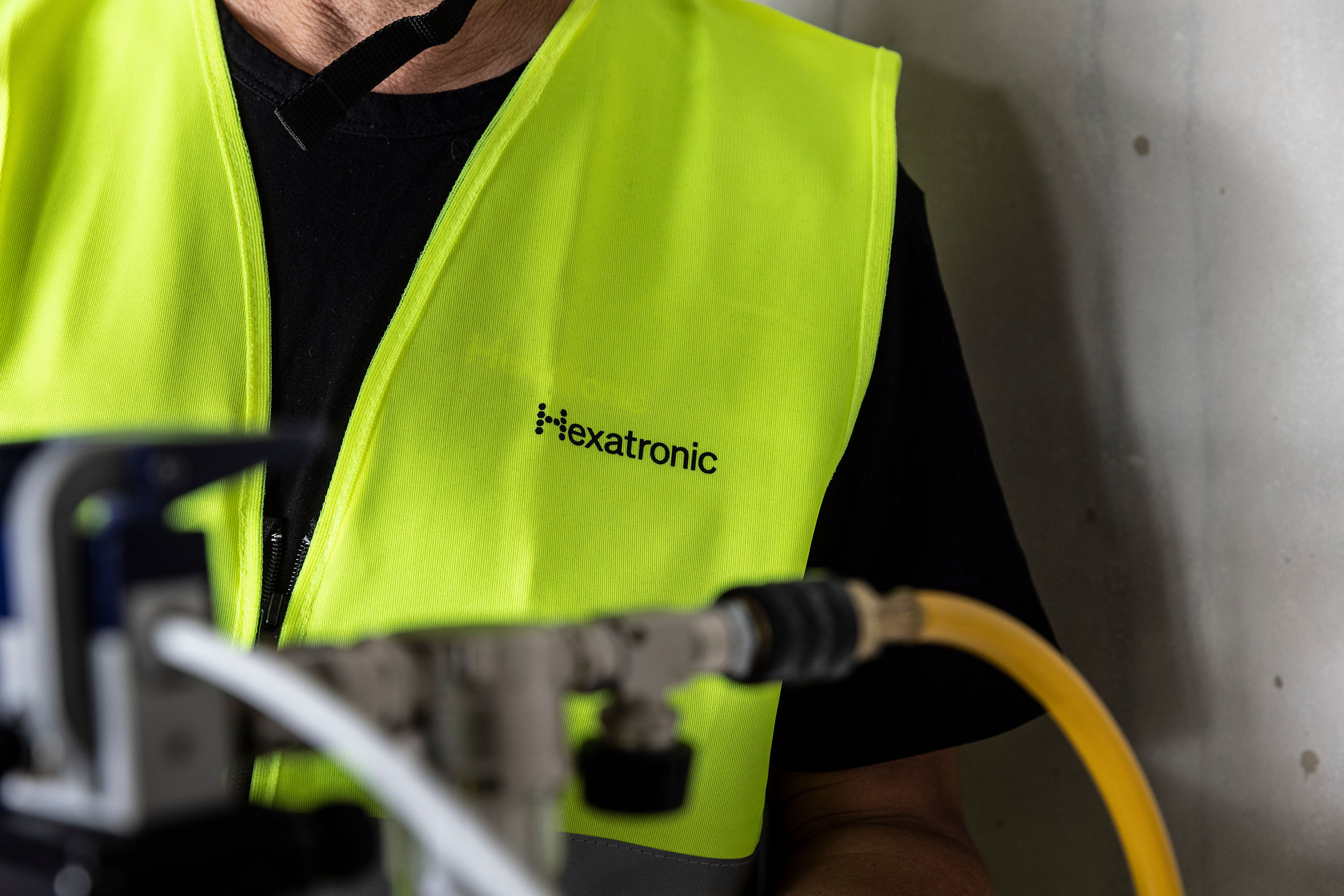 A person in a bright yellow safety vest marked “Hexatronic” is near machinery, indicating an installation work.