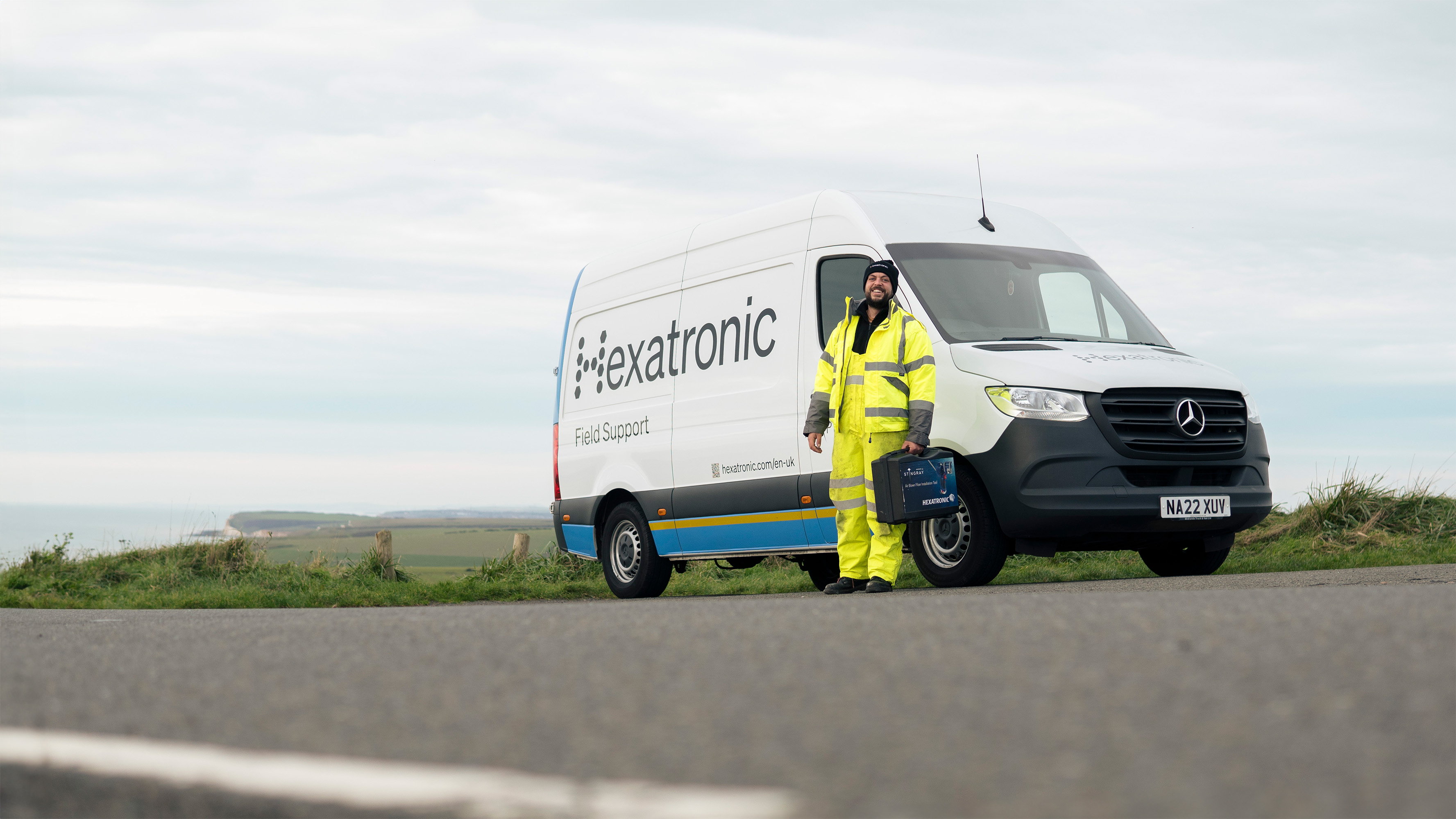 A person in a high visibility jacket stands in front of a Hexatronic van with a tool bag with the Stingray Air Blown Installation Tool in it.