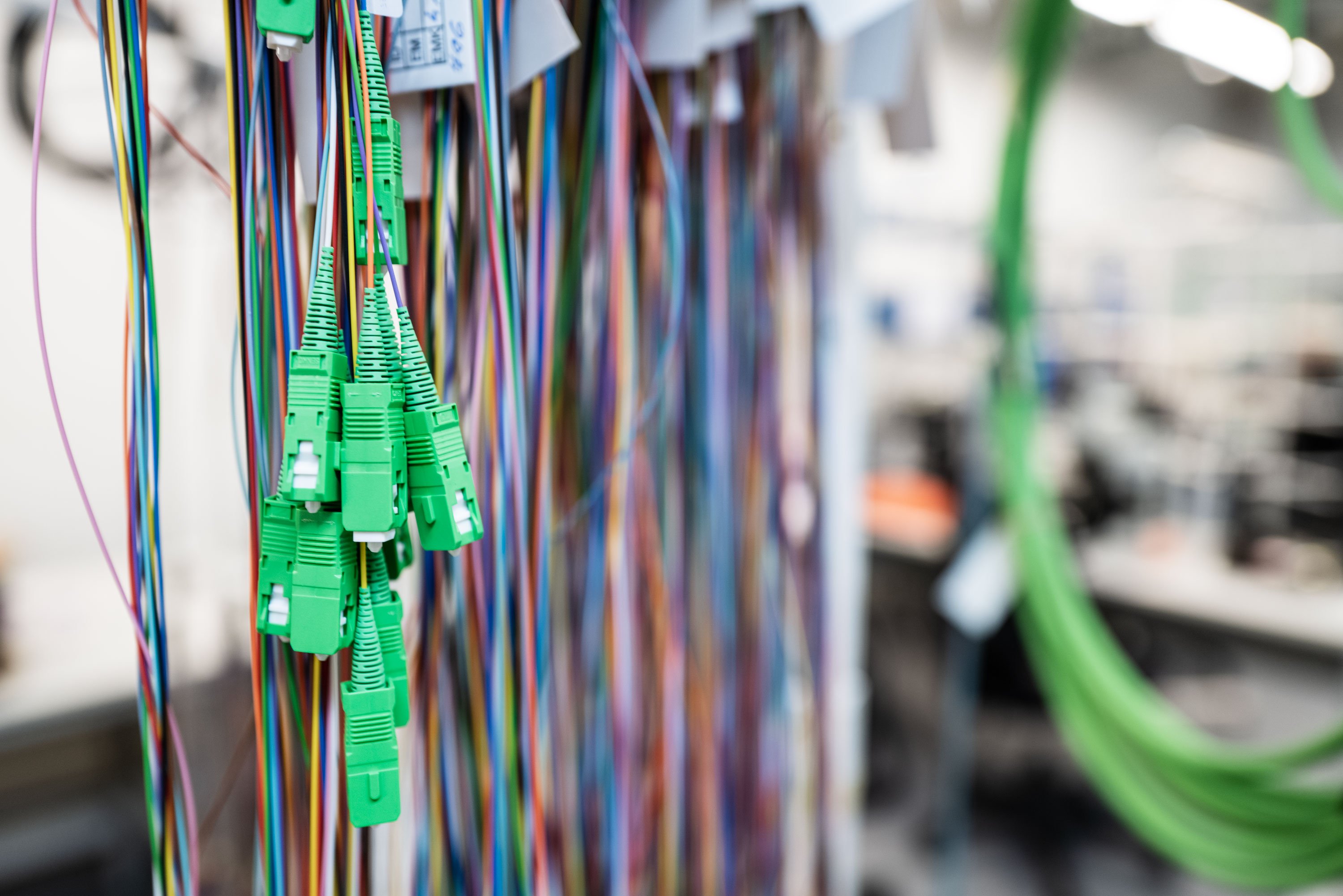 Cluster of colorful wires with green connectors, neatly organized and labeled, in a brightly lit workshop.
