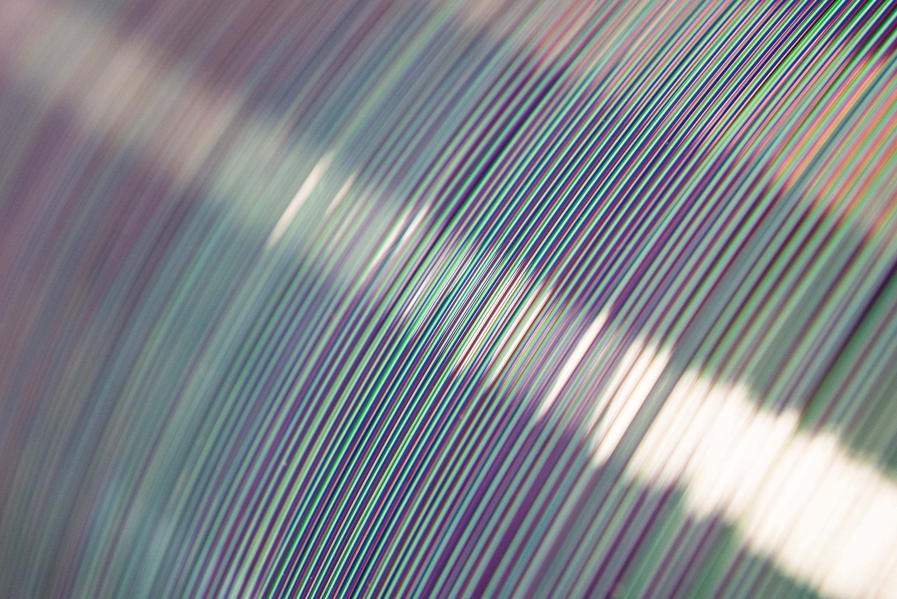Close-up of a curved surface with parallel lines in green, red, blue, and white, creating a textured pattern with light reflections.