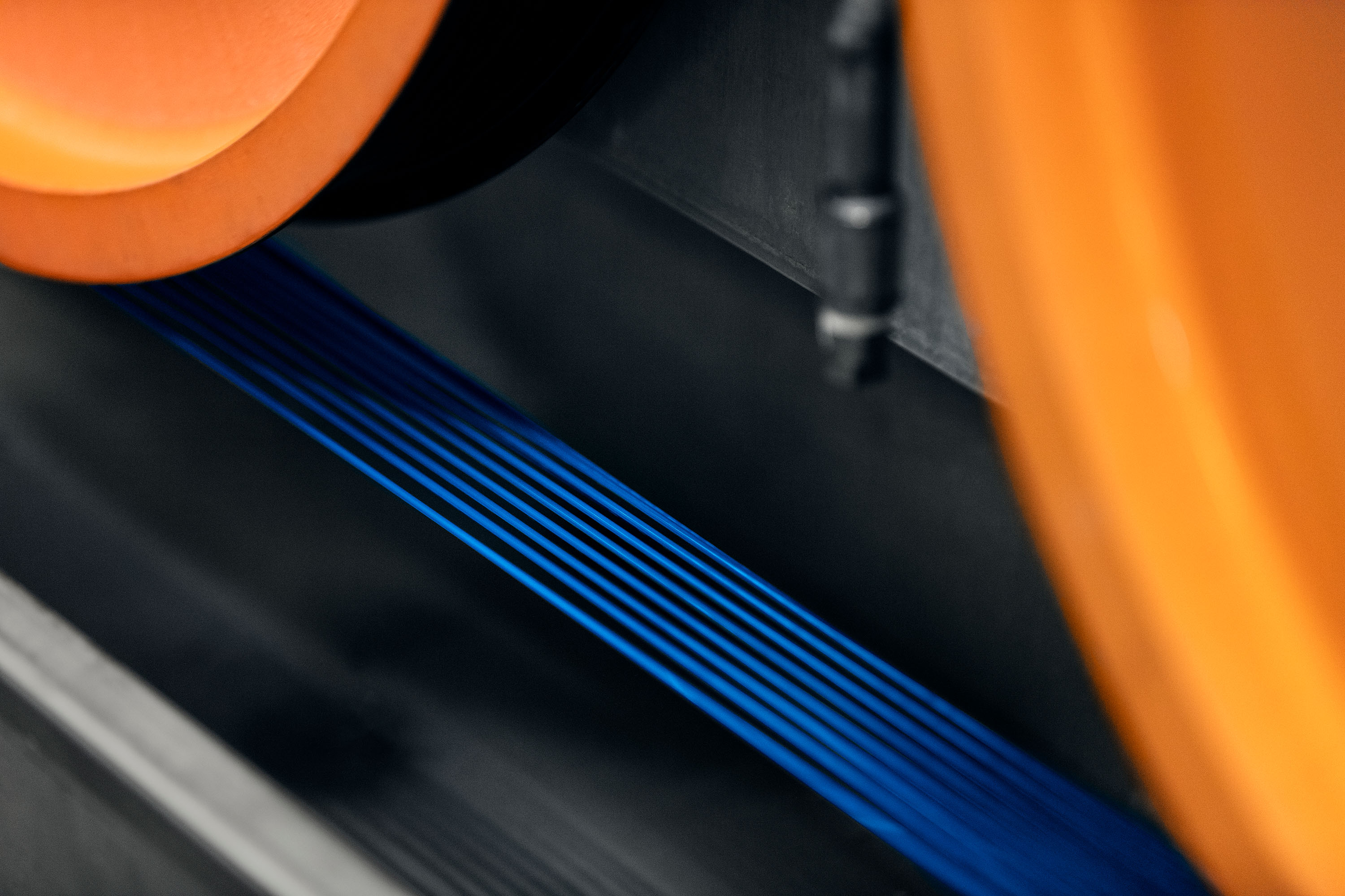 Close-up of blue optical fiber wires running through a machine line with orange tracked wheels.
