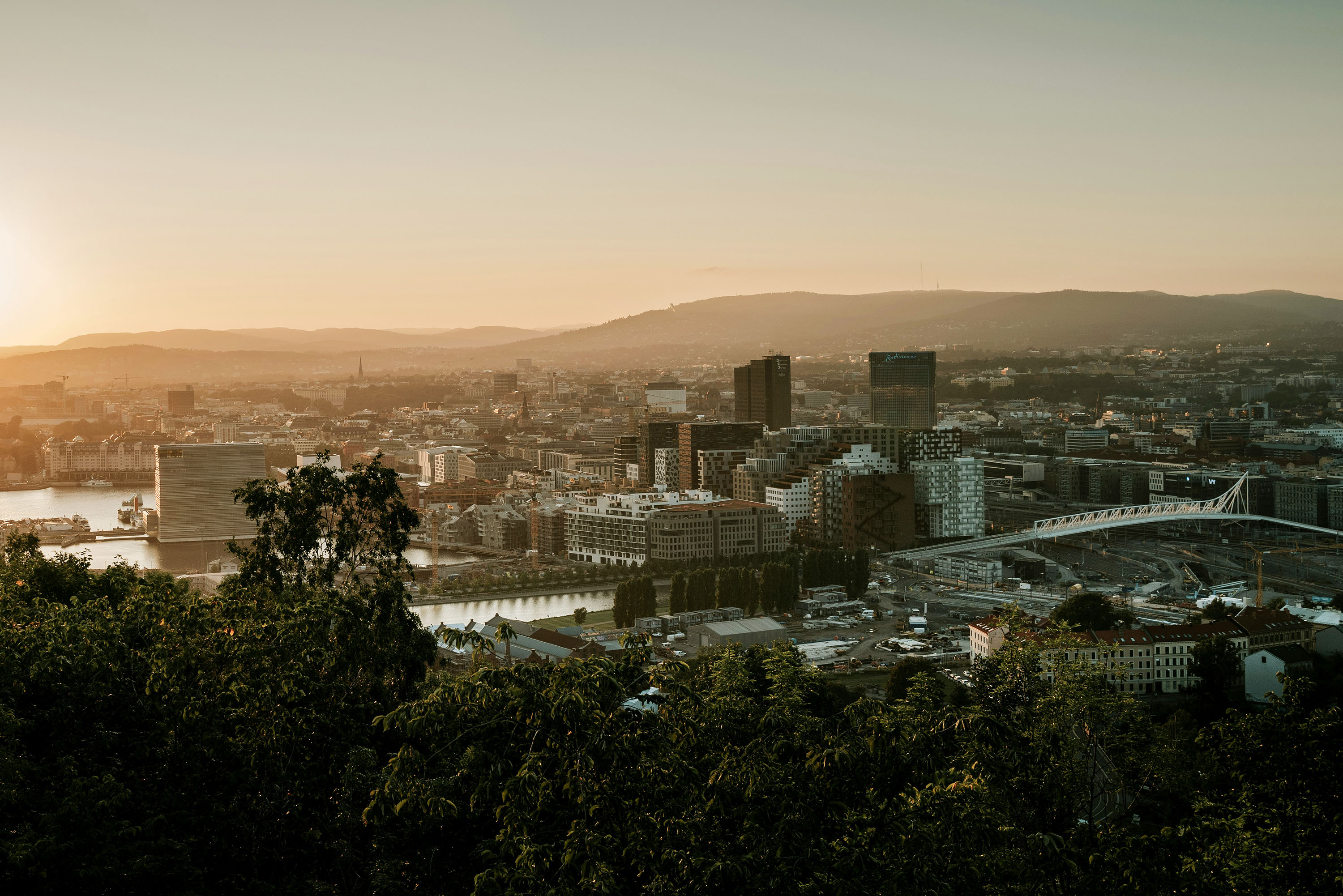 Aerial view of central Oslo at sunset with trees in the foreground.