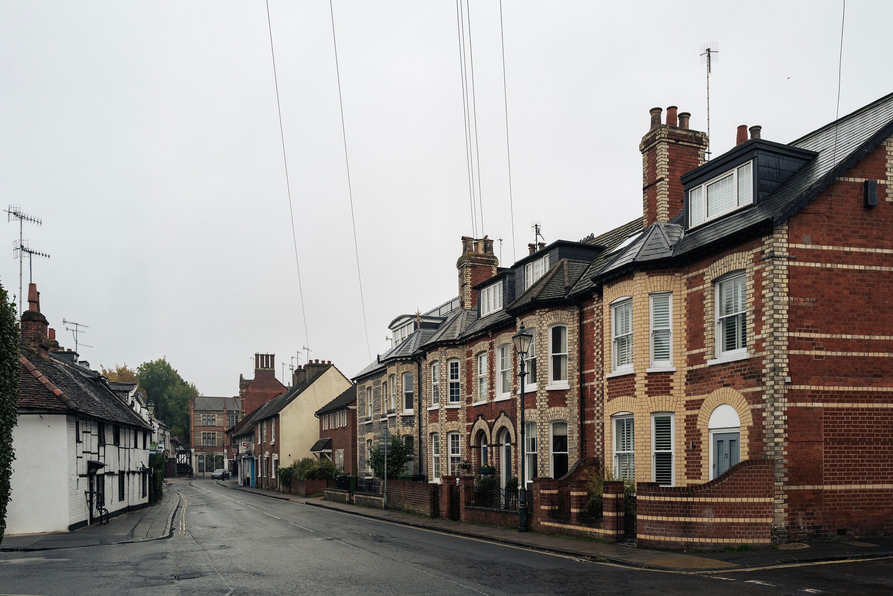 Misty street with traditional brick houses, wet road, no people or vehicles, overcast sky, serene and historical atmosphere.